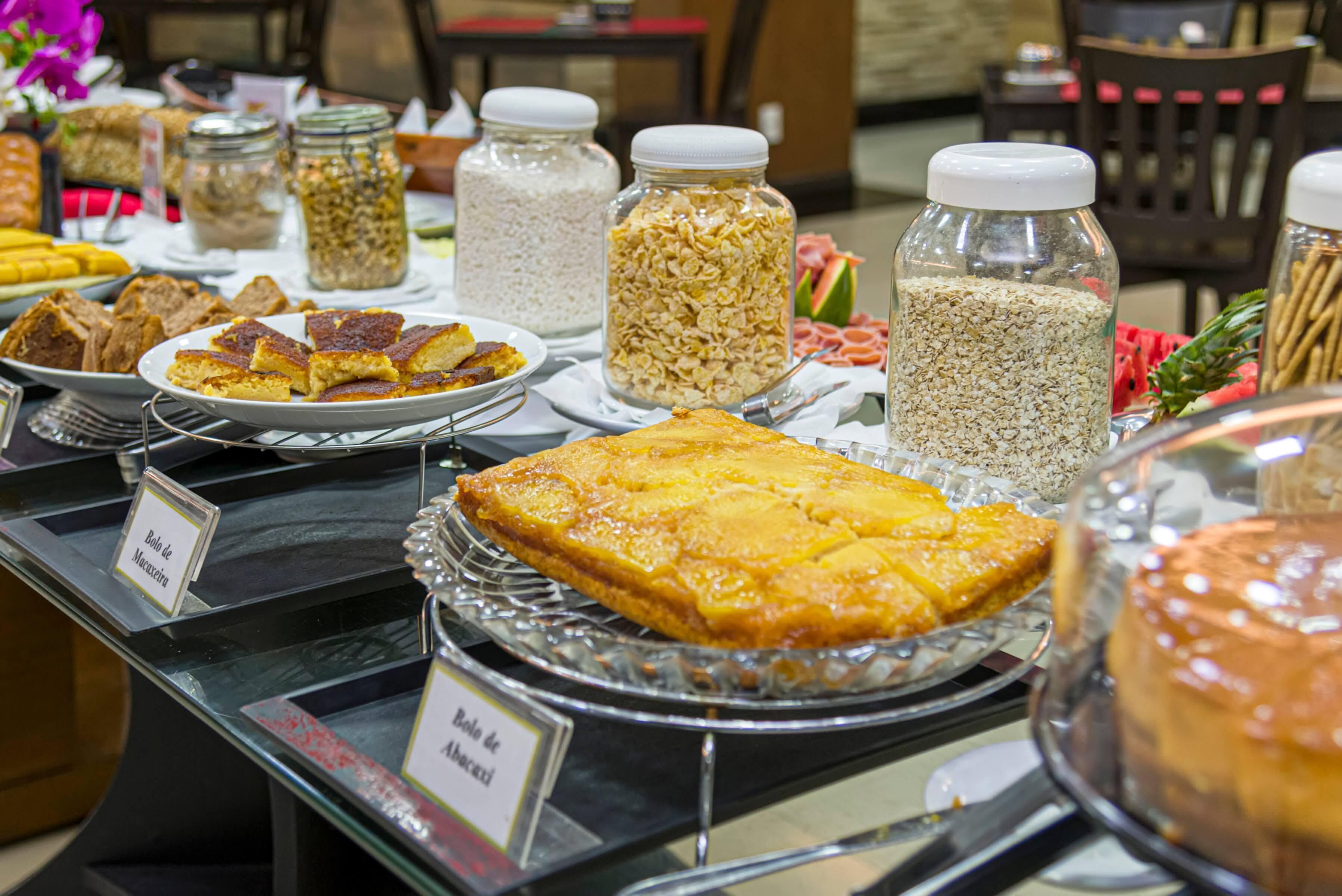 A buffet with various dishes and food items, including a large square cake and several jars of grains.