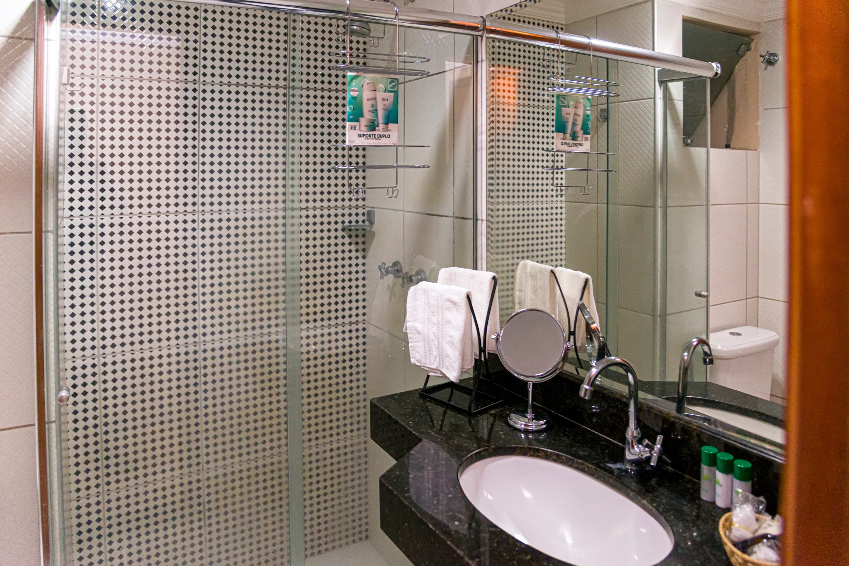 Un bany modern amb box dutxa de vidre, un lavabo amb mirall i articles de tocador al taulell.