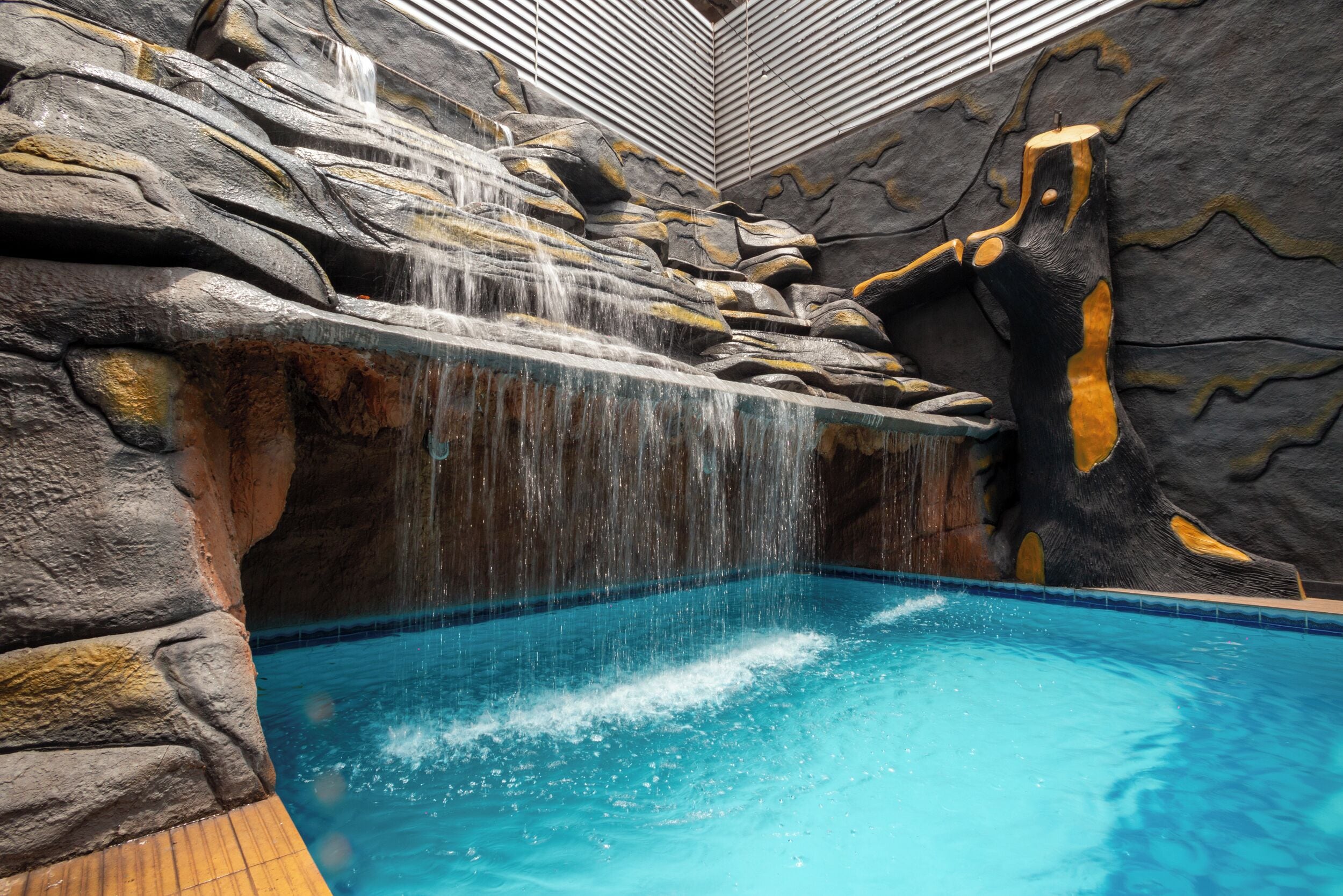 Une piscine agrémentée d’une cascade, entourée de murs qui ressemblent à des rochers.