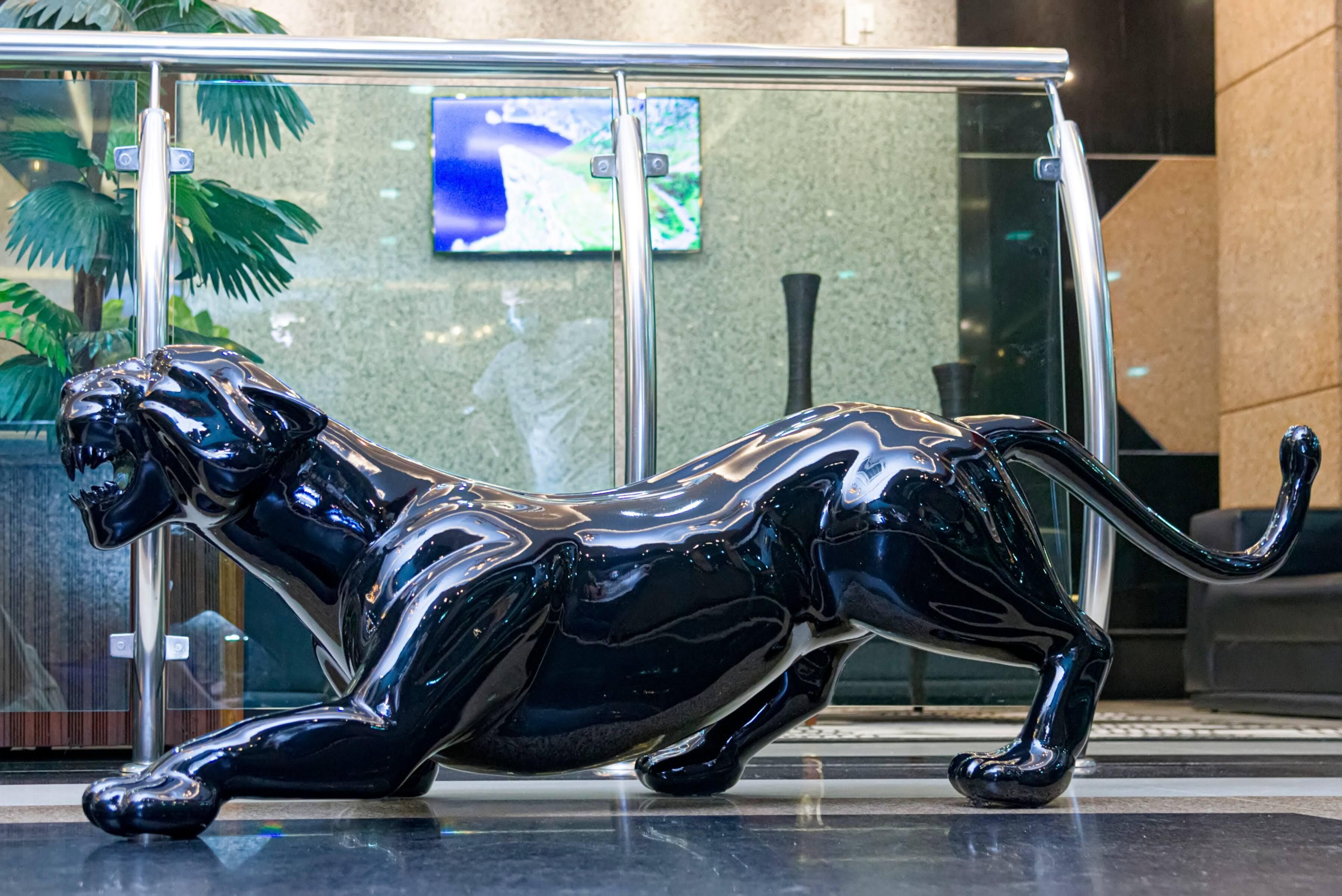 Una estàtua de pantera negra en un hall amb portes de vidre, una planta i una pantalla digital al fons.