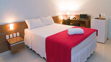 A hotel room with a bed, a desk, a chair, a laptop, and a refrigerator.
