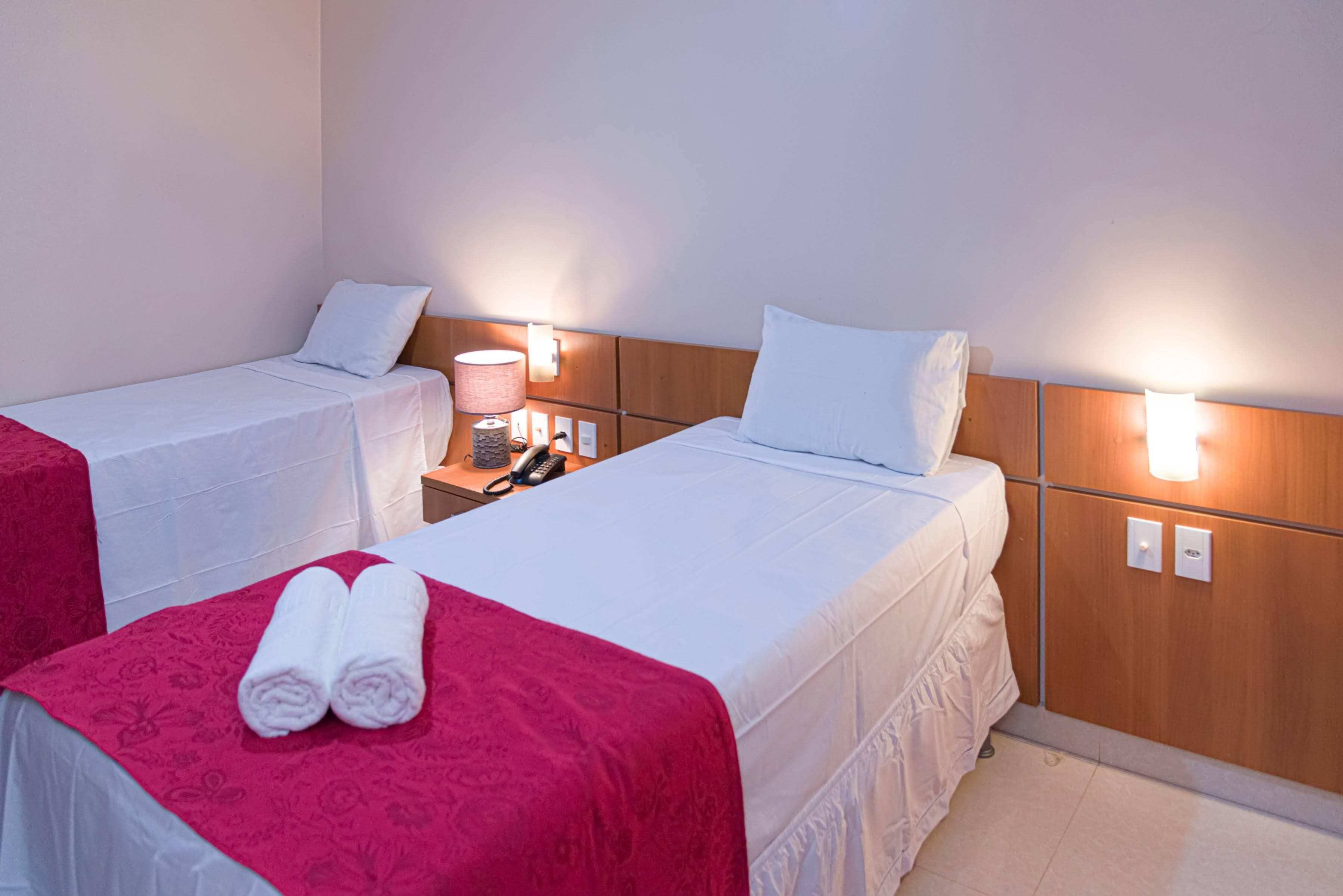 Habitación de hotel con dos camas, cada una con ropa blanca de cama y almohadas, cabeceros de madera, lámparas de noche y un teléfono en la mesita de noche.