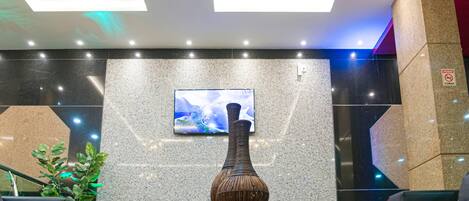 A lobby with a modern design, featuring a large vase on a table, a mounted TV, and a staircase.