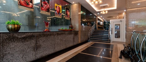 Un moderno vestíbulo de hotel con mostrador de recepción, obras de arte enmarcadas, una escalera y una barandilla de cristal.