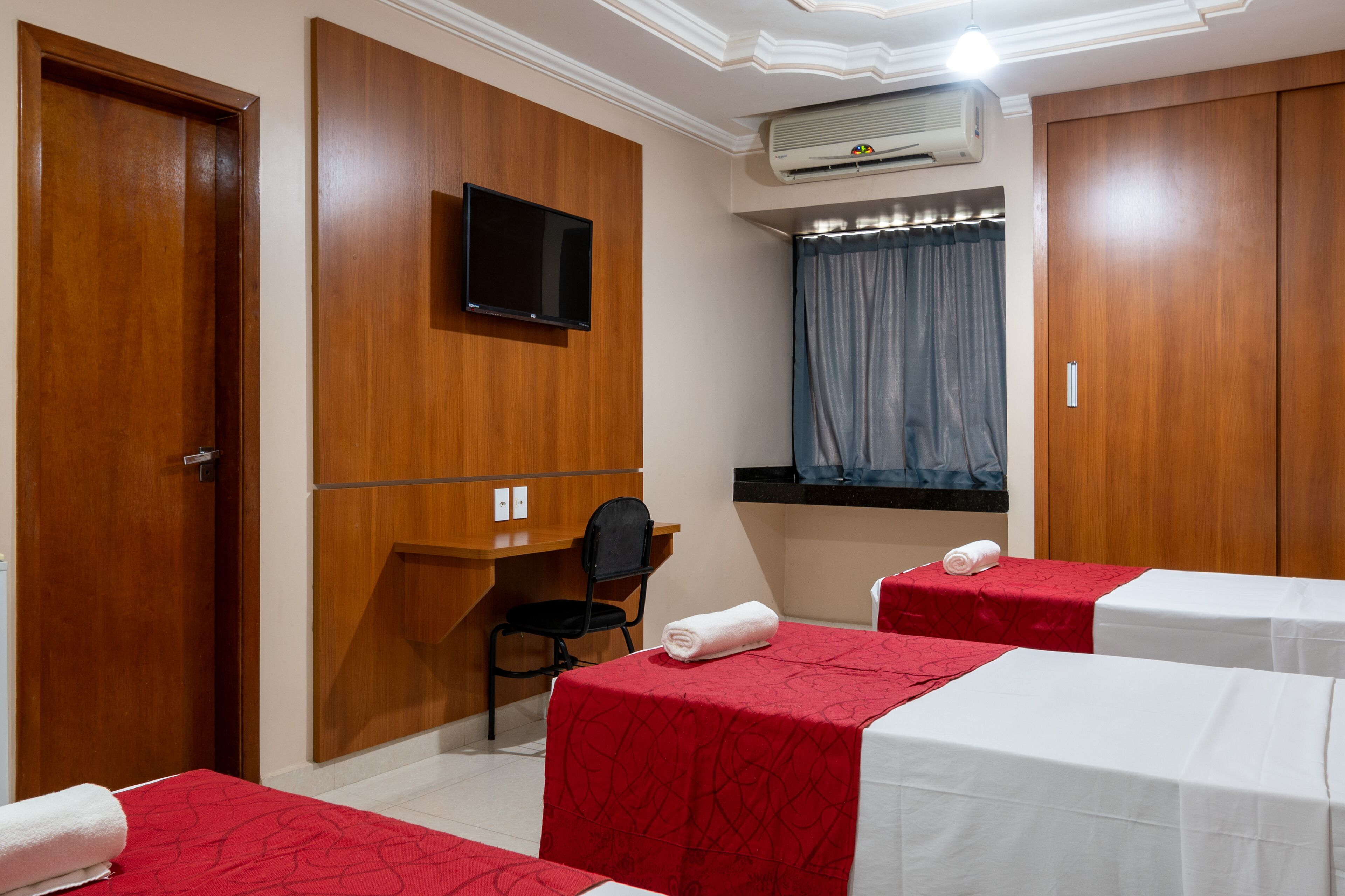 Een hotelkamer met twee bedden, een bureau, een stoel, een televisie en een airconditioner.