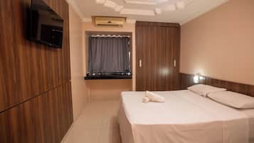 Habitación de hotel con una cama, un televisor de pantalla plana montado en la pared, una ventana con cortinas y un armario de madera.