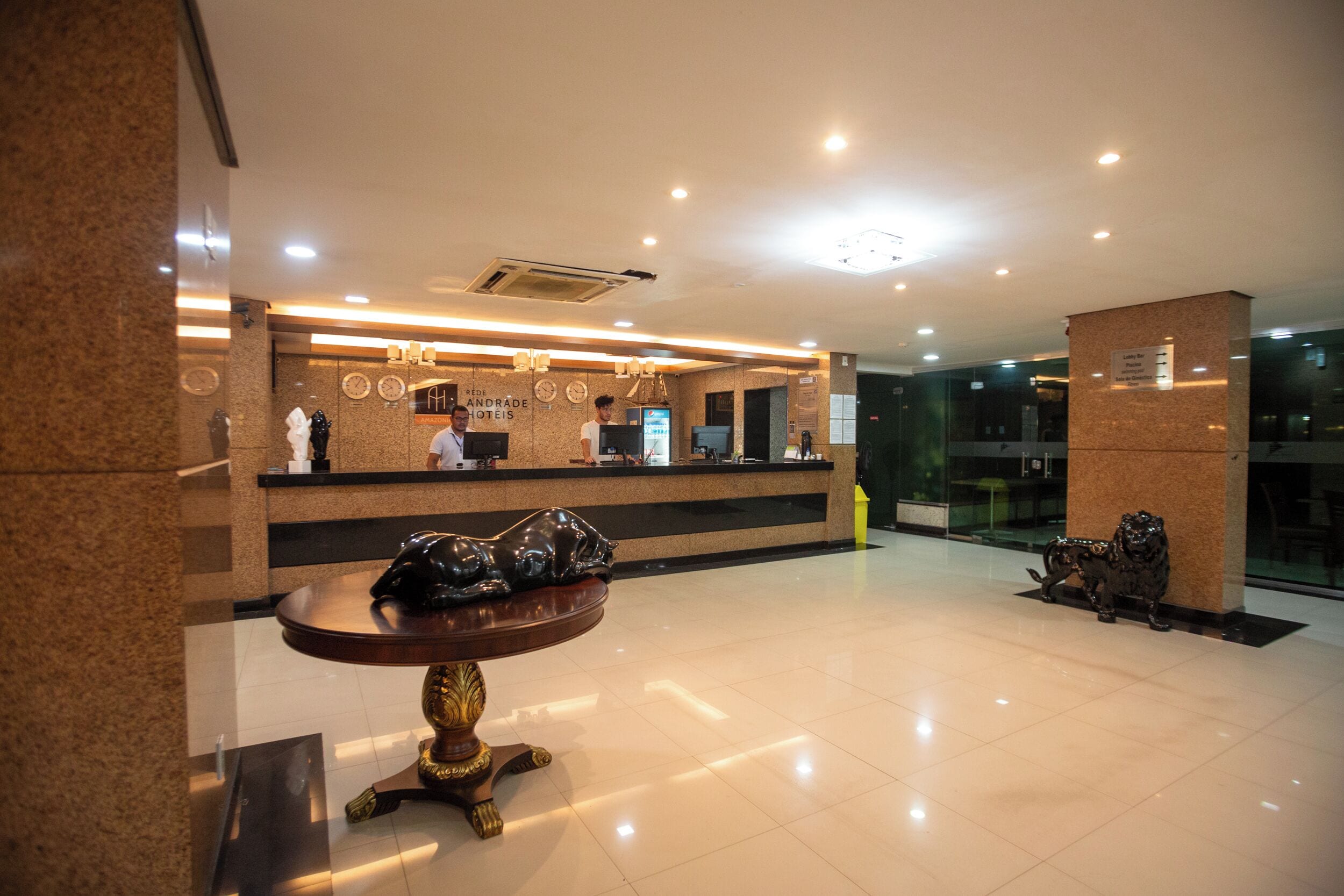 Zona de recepción de un hotel con mostrador, un reloj y una estatua de león.