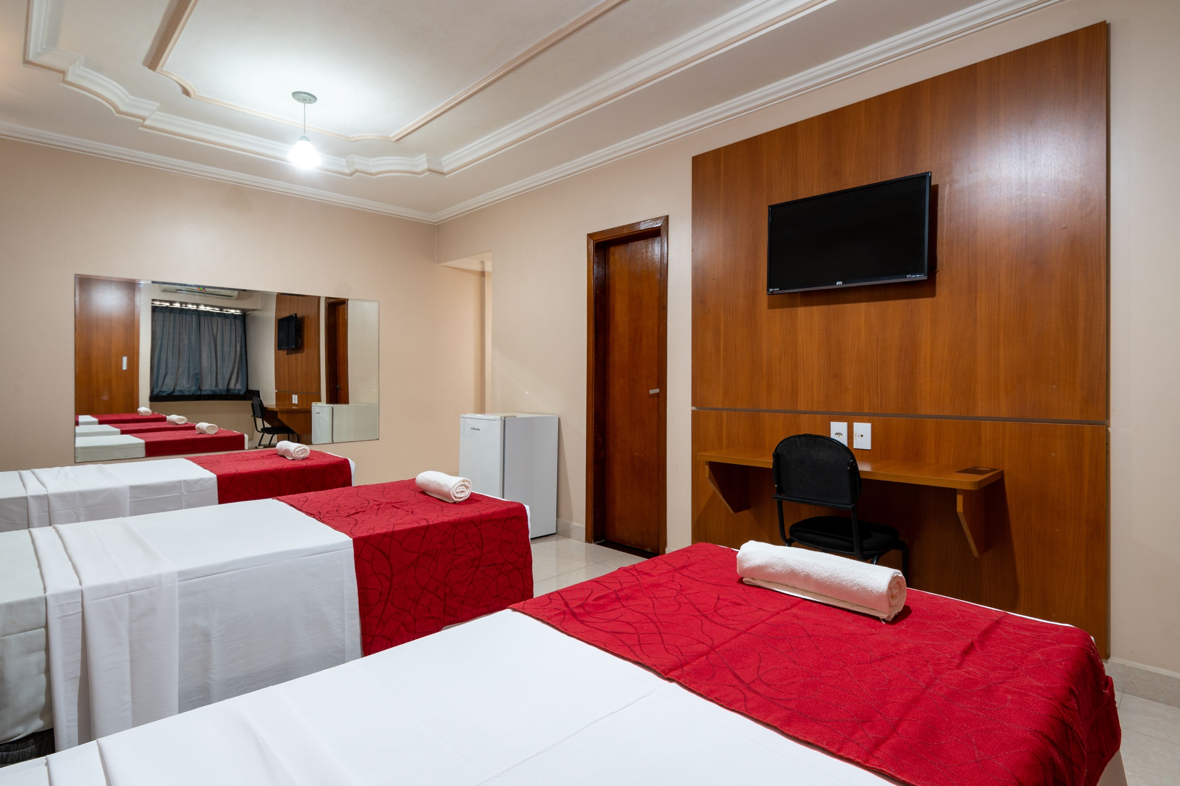 Ein Hotelzimmer mit zwei Betten, einem Fernseher, einem Schreibtisch und einem Spiegel.