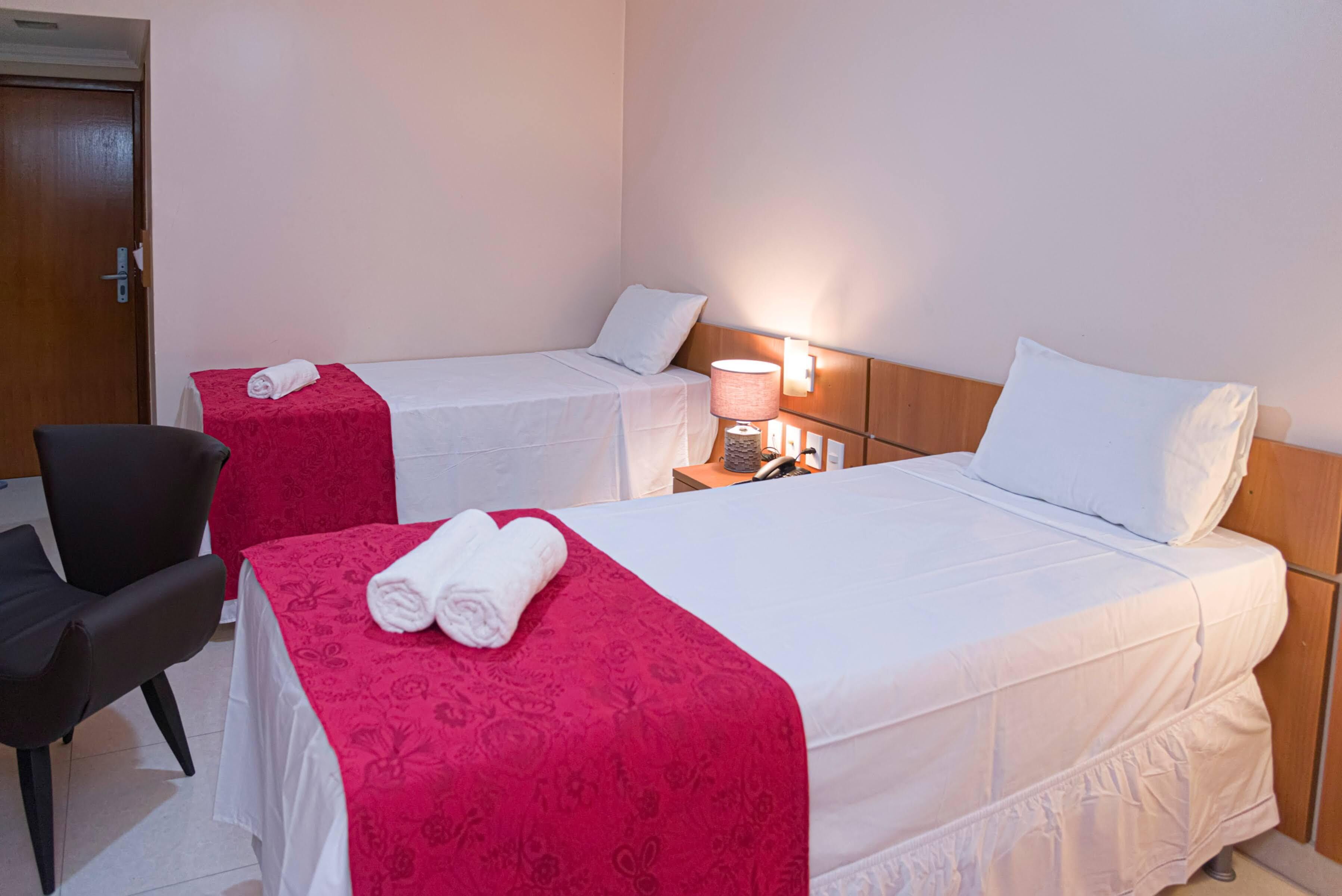 A hotel room with two beds, a chair, and a nightstand with a lamp.