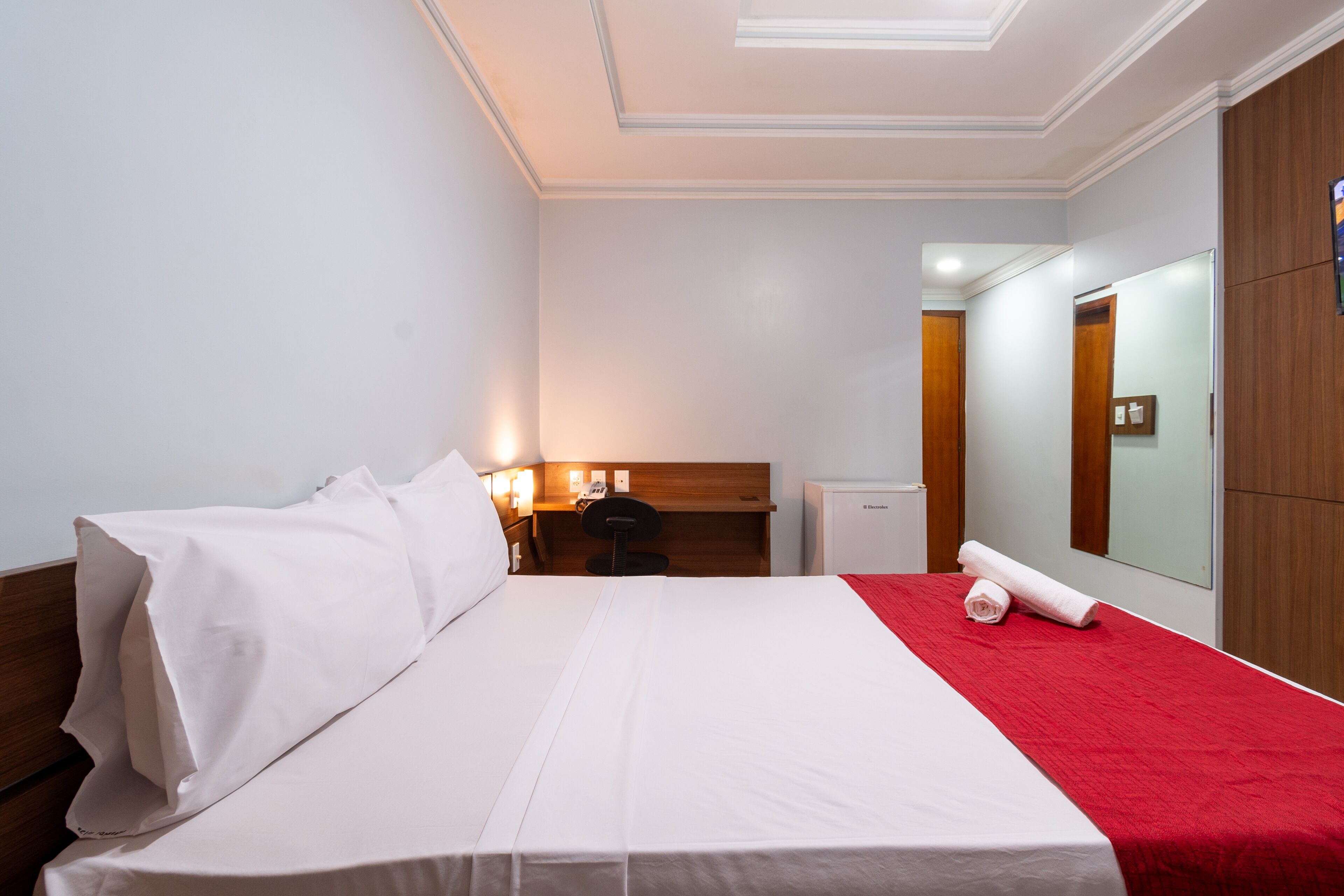 Een hotelkamer met een groot bed, een bureau, een stoel, een spiegel en een kledingkast.
