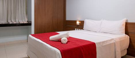Ein ordentlich bezogenes Bett mit roter Decke, einem hölzernen Kopfteil und einem Nachttisch mit Lampe.
