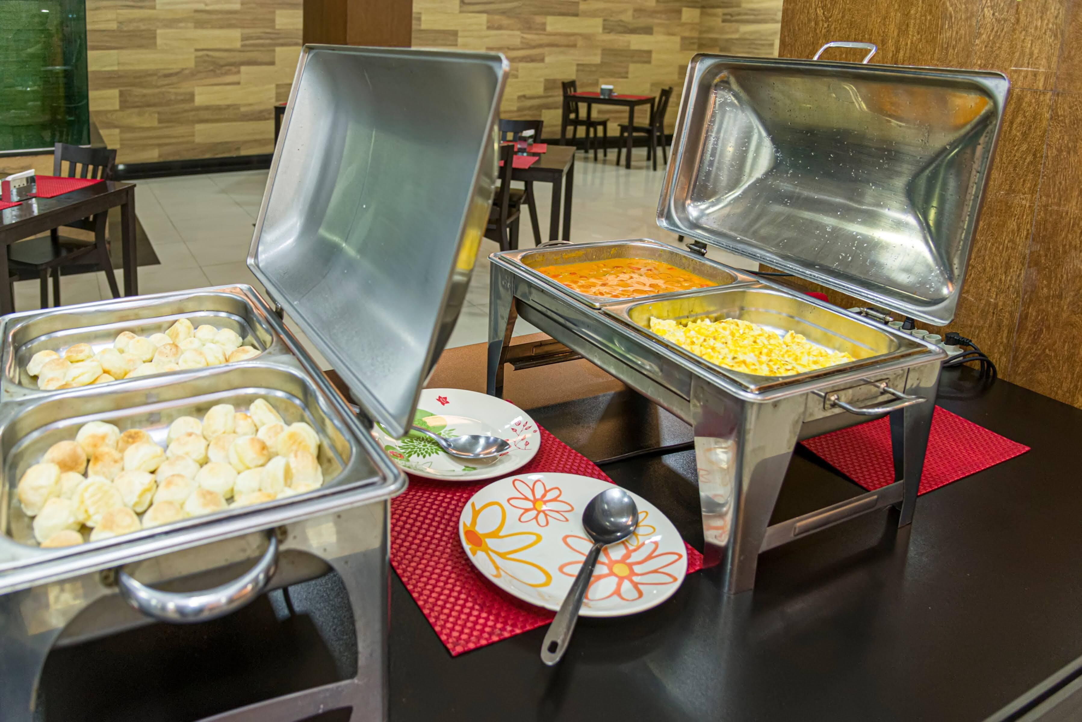 A buffet setup with various food items in metal containers, a spoon, and a plate with a floral design.