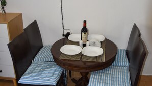 Un área de comedor con una mesa redonda, dos sillas, un televisor montado en la pared y una botella de vino sobre la mesa.