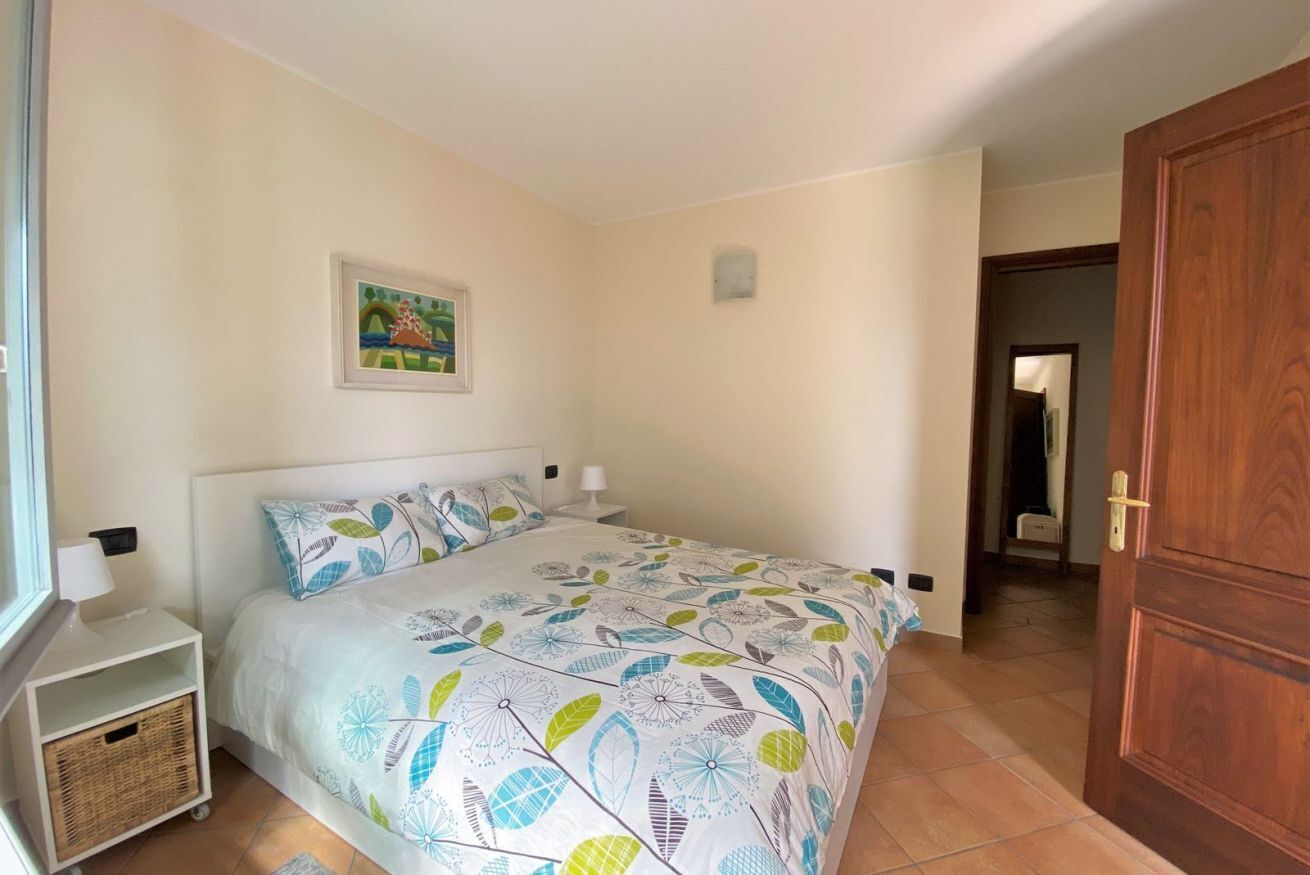 A bedroom with a bed, a nightstand, a bedside table, a wall-mounted picture, and a wooden door.
