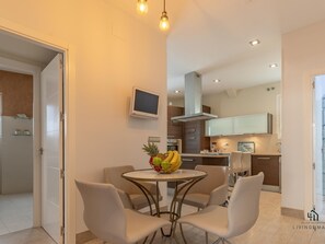 Una cocina moderna con zona de comedor, que incluye una mesa redonda con sillas, un frutero y un televisor en la pared.