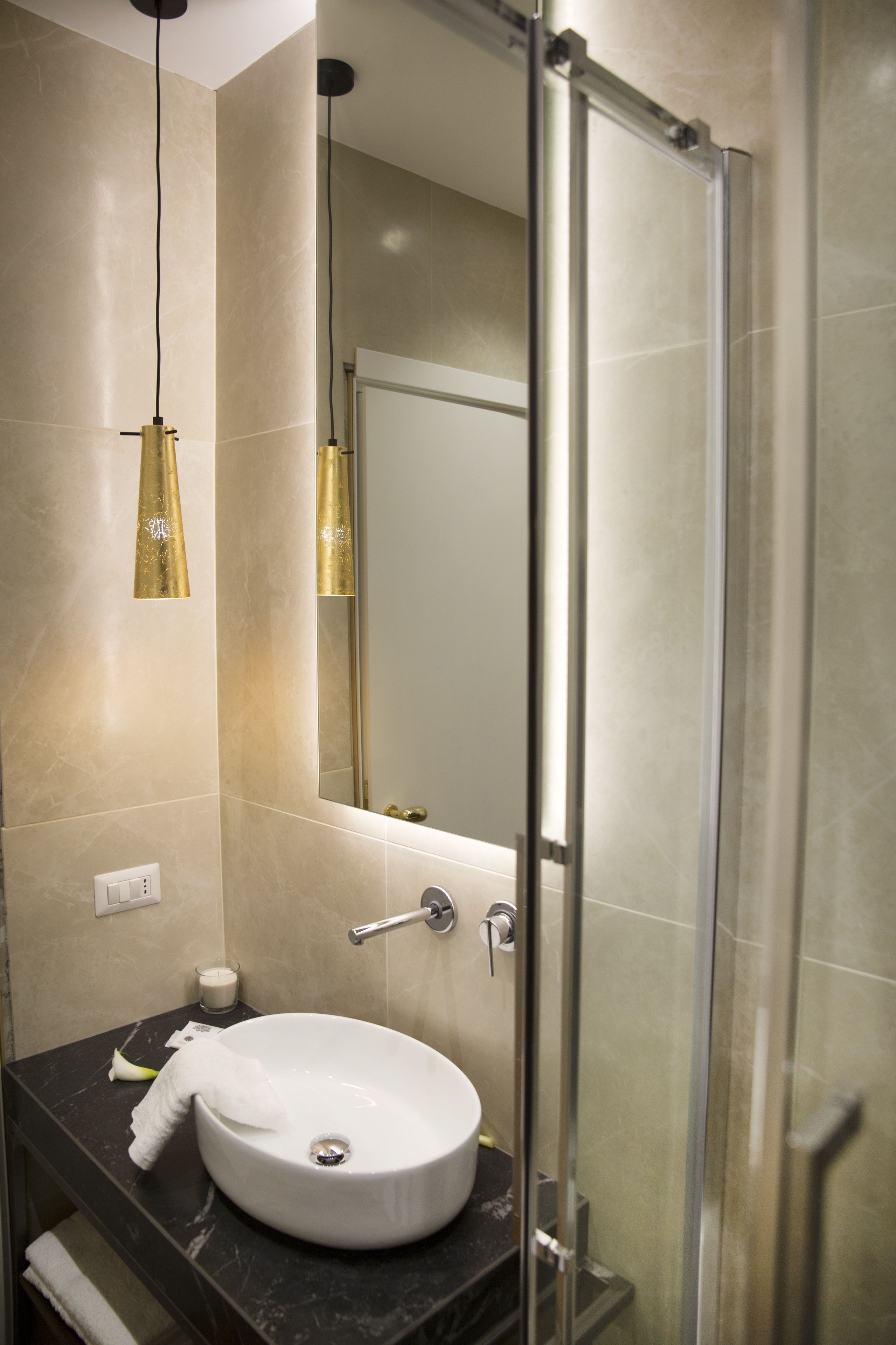 A modern bathroom with a glass shower enclosure, a white sink, and gold pendant lights.