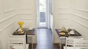 A narrow hallway with two dining areas, each with a table set for two, white chairs, and a view into a bright room through a door. - Unicum Roma Suites (Rome)