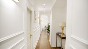 A hallway with white walls, wooden flooring, and a desk with a lamp. - Unicum Roma Suites (Rome)