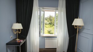 A room with a window, a radiator, a table with a lamp, and a floor lamp. - Unicum Roma Suites (Rome)