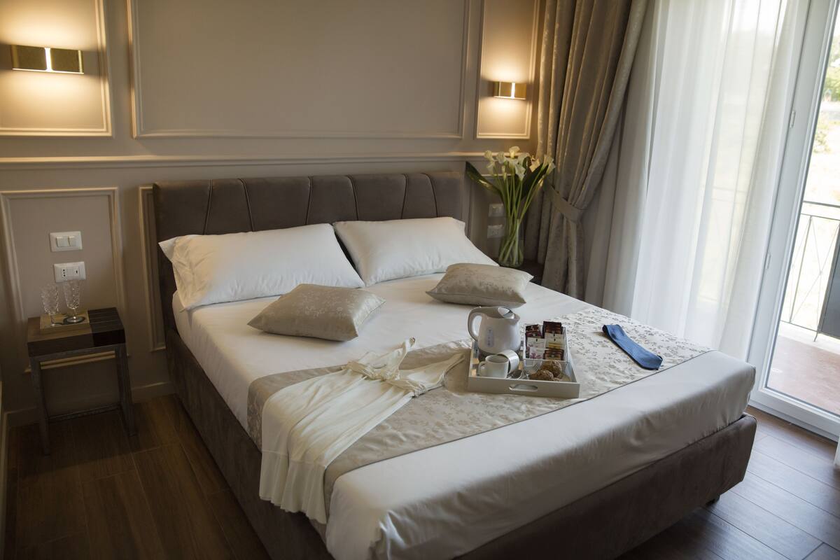 A neatly made bed with pillows, a tray with a cup and snacks, and a vase of flowers.