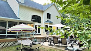 A large house with a covered patio area, outdoor seating, and a hammock. - Experience luxury at Riverwalk, a 4-bedroom retreat in serene Saugatuck, MI. (Saugatuck)
