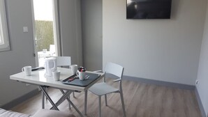 Una habitación moderna y minimalista con una mesa blanca, dos sillas, una cafetera y un televisor de pantalla plana montado en la pared.