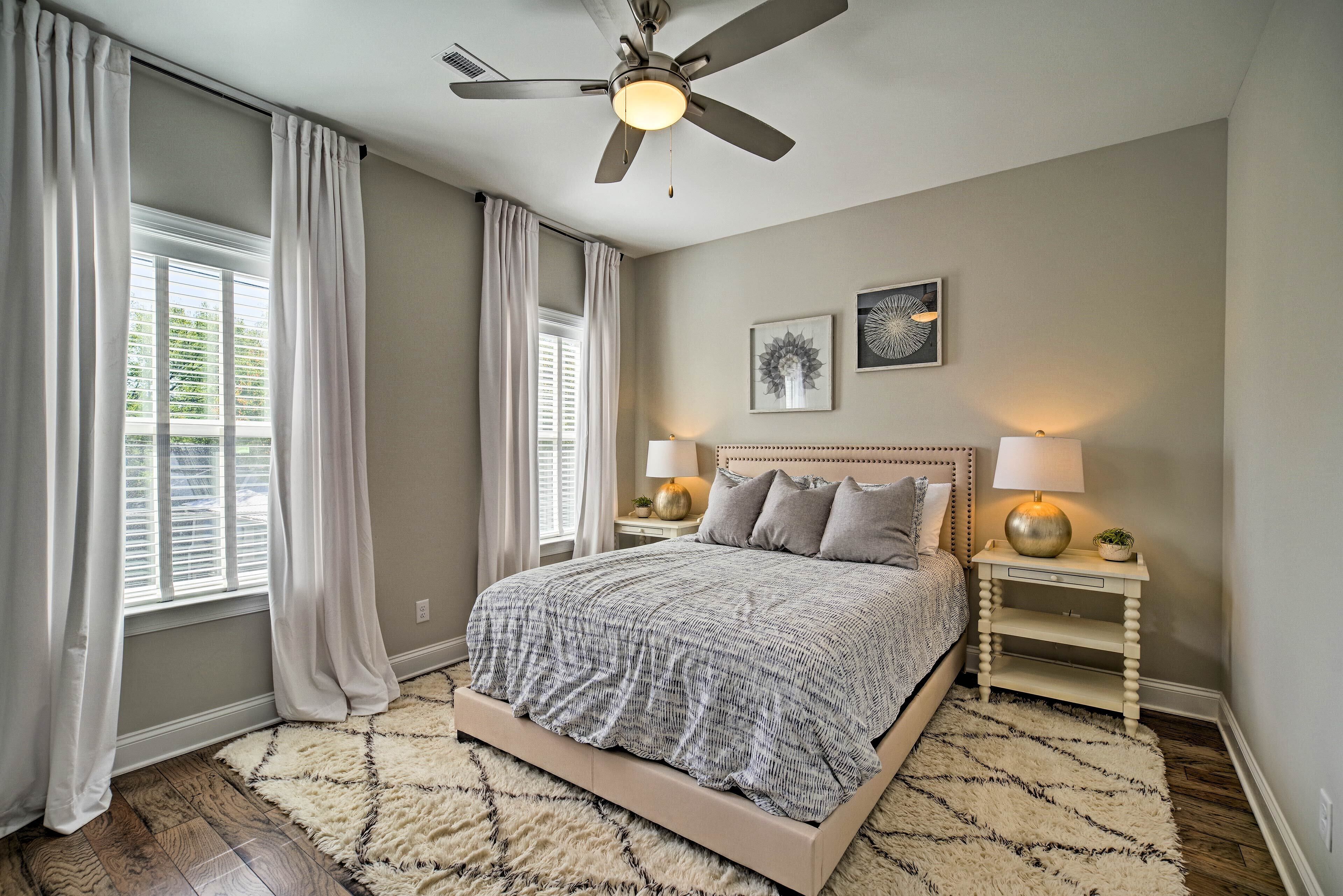 A bedroom with a bed, two bedside tables with lamps, a ceiling fan, and a window with curtains.