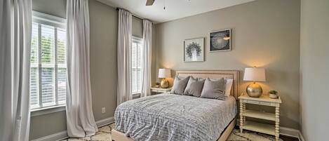 A bedroom with a bed, two bedside tables with lamps, a ceiling fan, and a window with curtains.