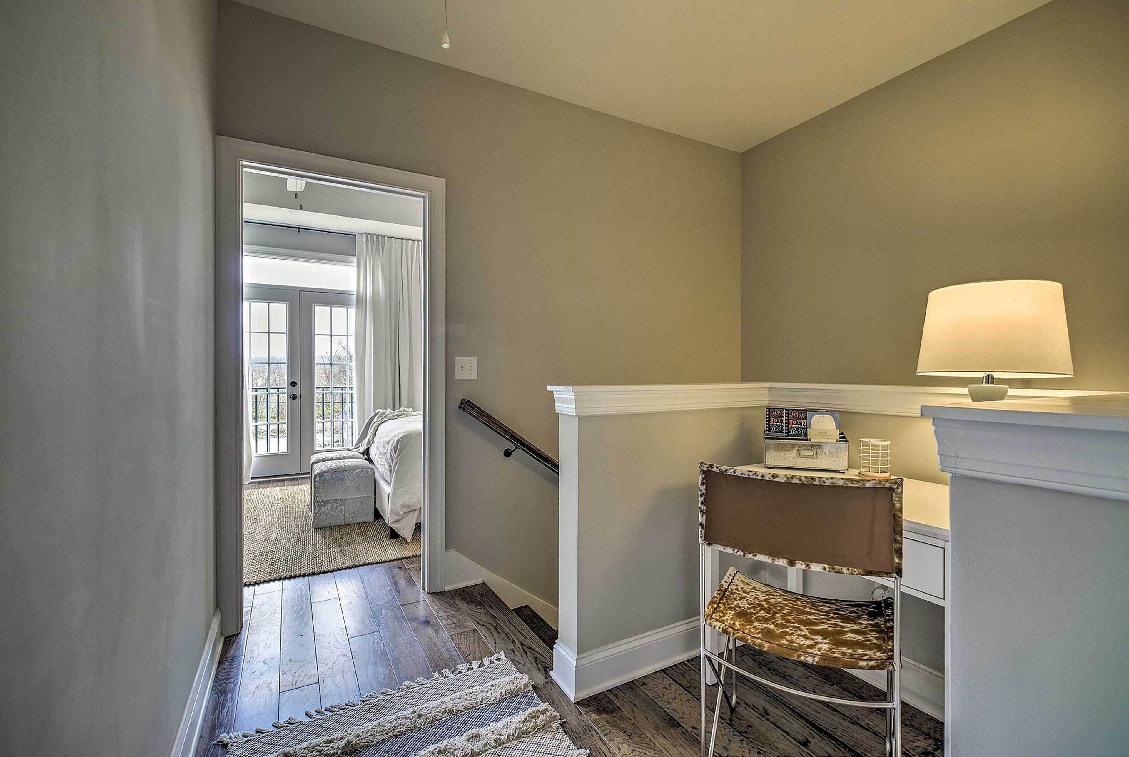 A hallway with a staircase leading to a balcony, a chair, and a table with a lamp.