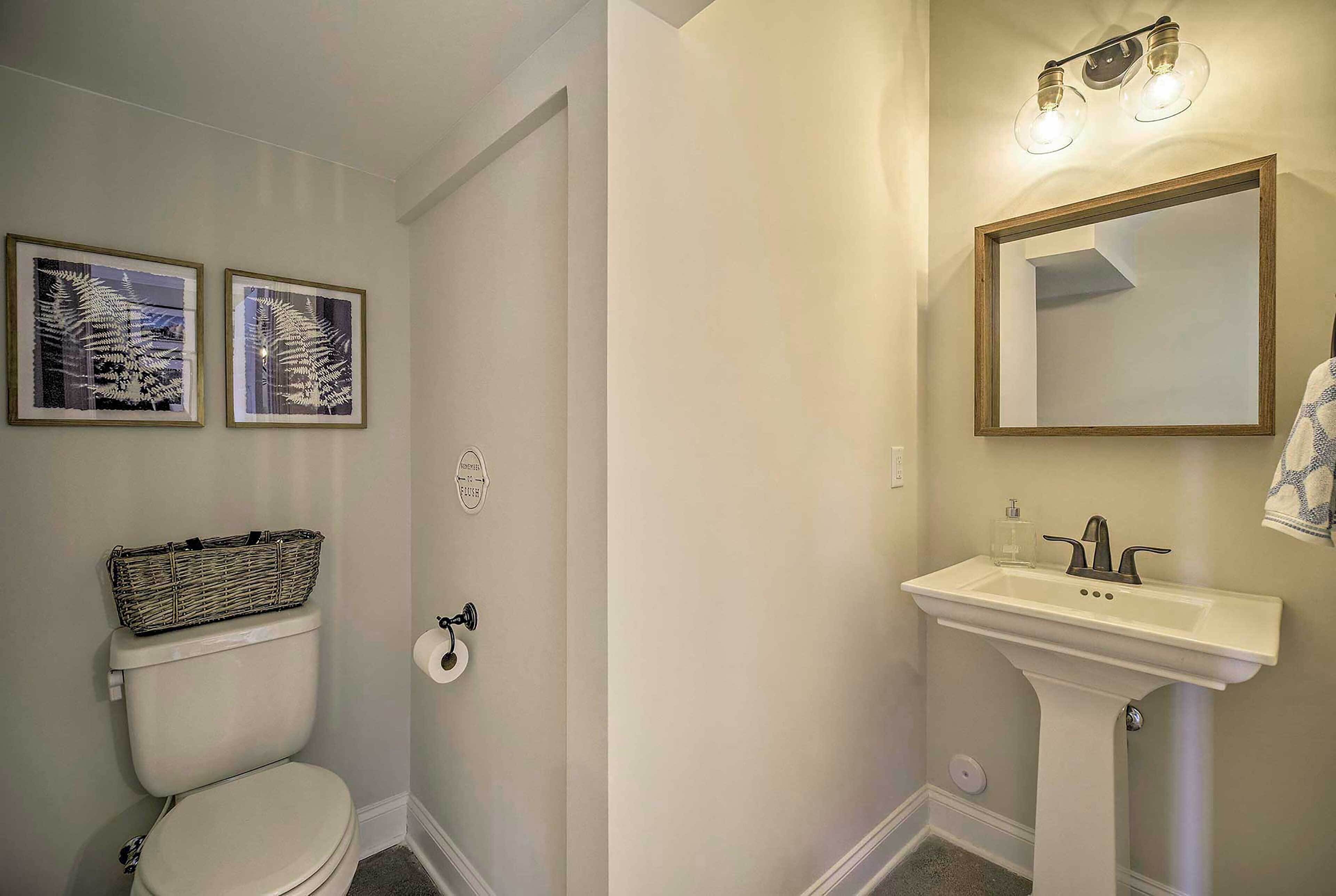Une salle de bain comprenant des toilettes, un lavabo avec un miroir et deux œuvres d’art encadrées accrochées au mur.