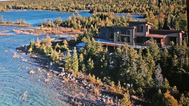 A modern cabin with a large deck overlooking a lake surrounded by dense forest.