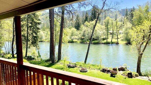 A wooden deck overlooking a river with trees and a grassy area.