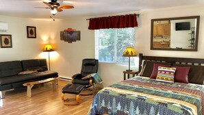A bedroom with a bed, a chair, a sofa, a lamp, a ceiling fan, and a window with blinds.