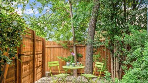 A wooden fence, a table with chairs, and a tree in a garden area. - Walk to Restaurants & Shopping; 1 mile to SoCo (Austin)