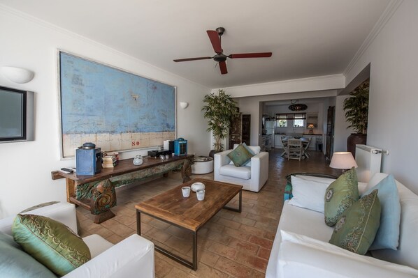 A spacious living room with a large blue artwork, a wooden coffee table, white sofas, and a ceiling fan. - Apt. Al-Gharb, just across Meia Praia Beach (Lagos)
