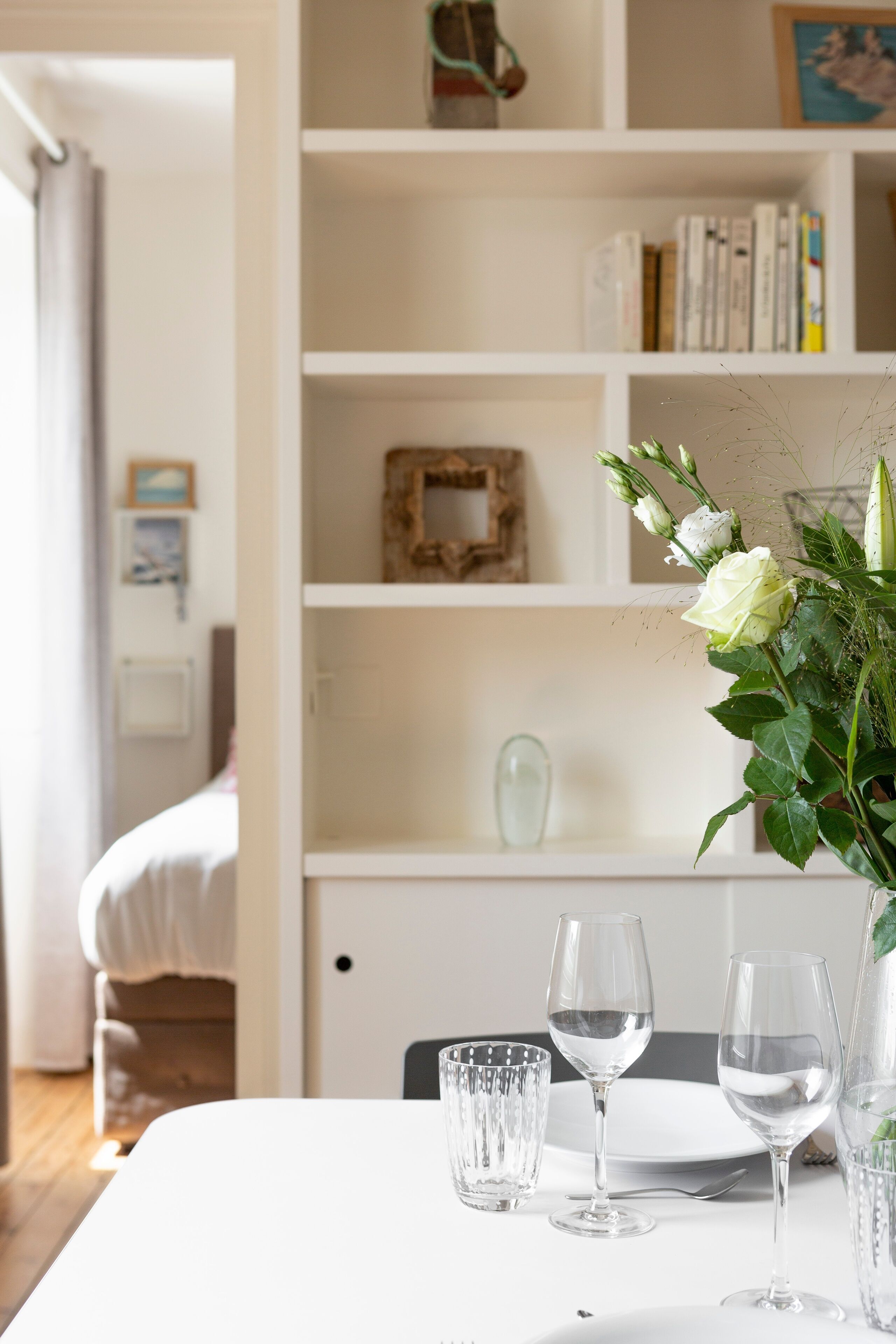 Ein Esstisch mit klaren Gläsern und einer Blumenvase, im Hintergrund ein Bücherregal.