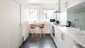 Una cocina moderna con armarios blancos, un microondas negro, un hervidor y dos taburetes de bar de madera.