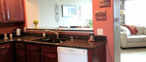 A kitchen with dark wood cabinets, a white dishwasher, and a granite countertop.