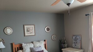 Een slaapkamer met een bed, nachtkastjes, een dressoir, een plafondventilator en wanddecoraties.