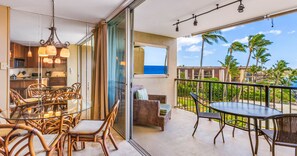 Ein Balkon mit Korbmöbeln, einem Glastisch und Blick aufs Meer.