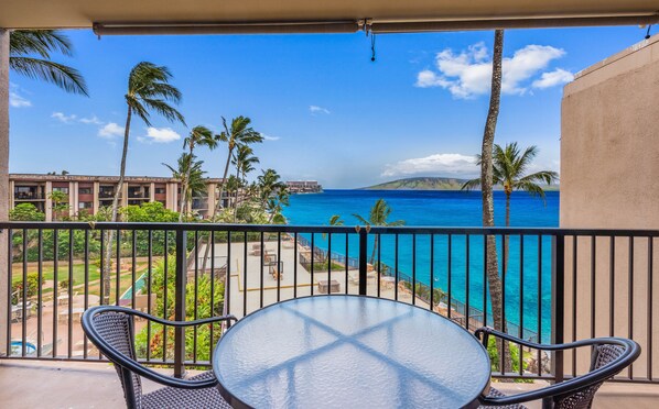 Ein Balkon mit Blick auf das Meer, Palmen und ein Gebäude im Hintergrund.