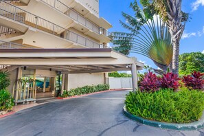 Ein mehrstöckiges Hotel mit überdachter Einfahrt, einer Palme und verschiedenen Pflanzen.