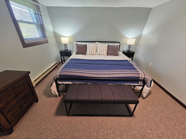 A bedroom with a bed, bedside tables, a bench, and a dresser.