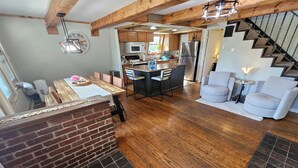 Une cuisine spacieuse avec un plancher en bois, un coin repas agrémenté d’un mur en briques apparentes et un escalier menant à un autre niveau.