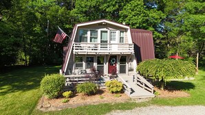 Une maison à deux étages avec un porche, un drapeau et une boîte aux lettres.