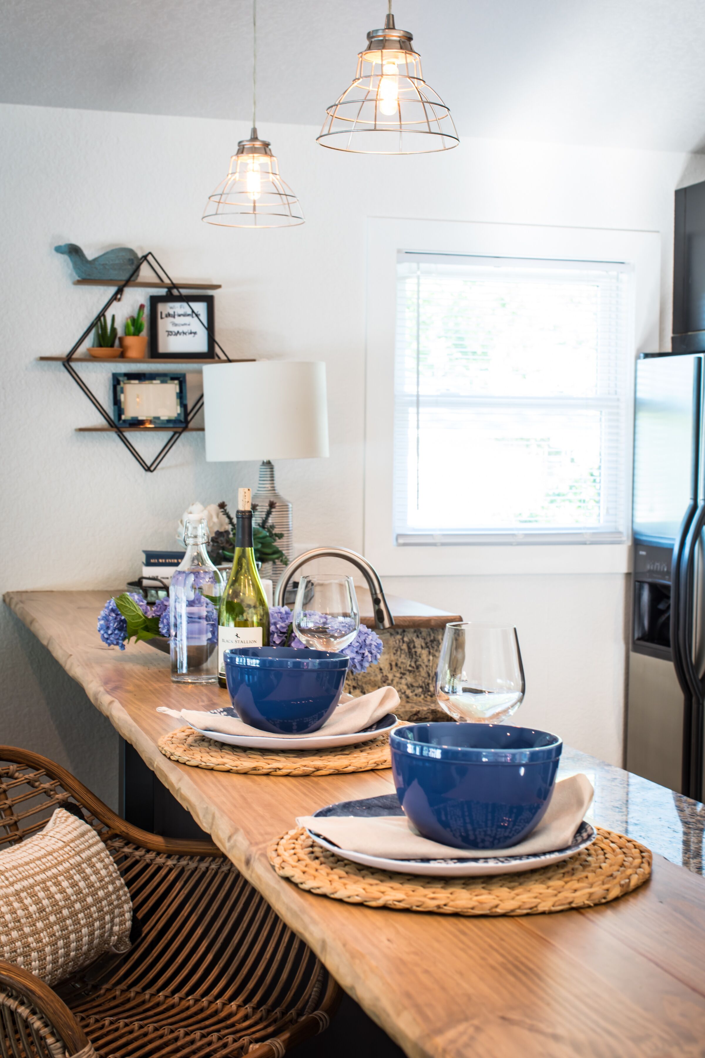 A kitchen with a wooden countertop, two hanging pendant lights, and a window with blinds.