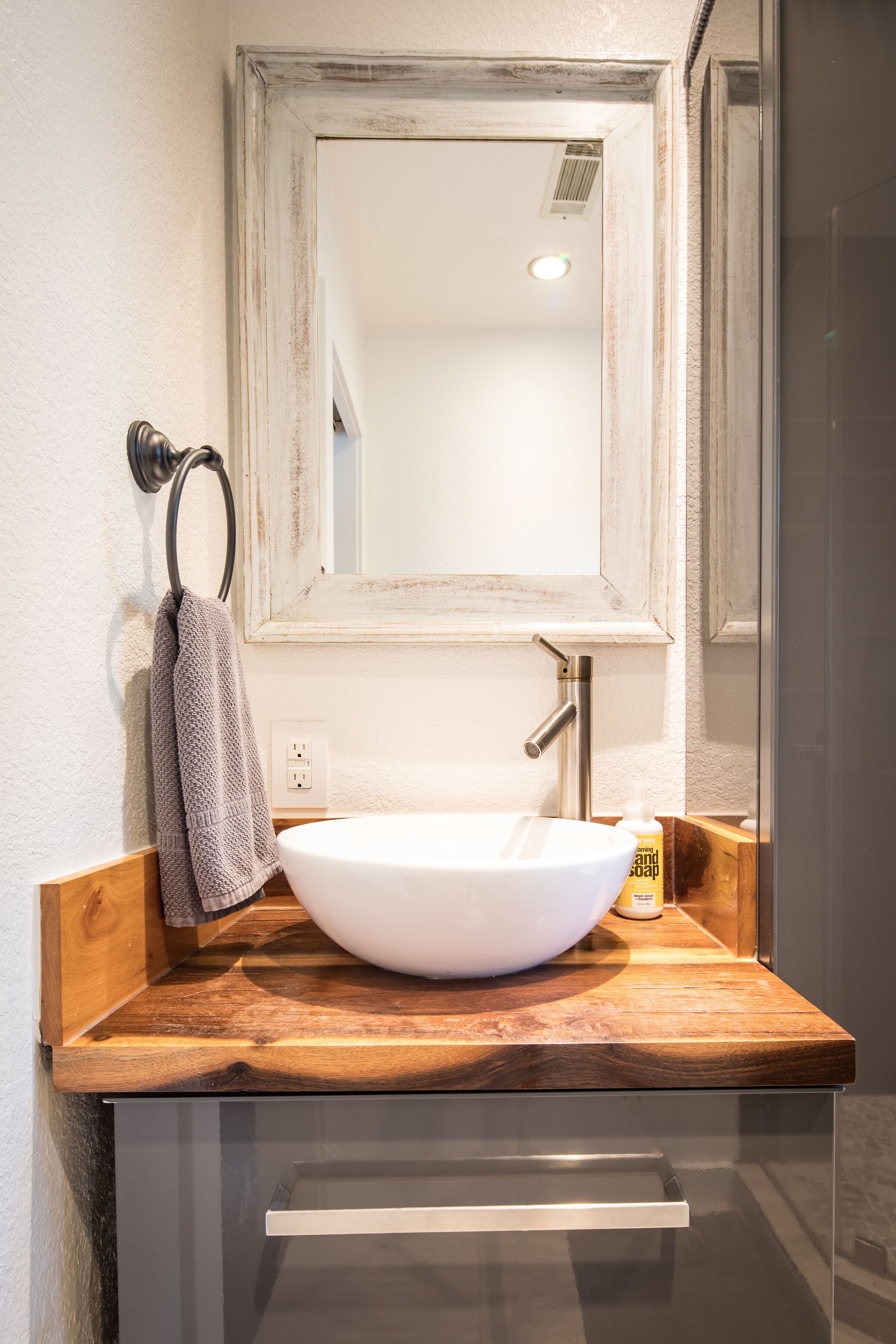 Un baño con un lavabo blanco, una encimera de madera, un espejo y una toalla colgada en un aro metálico.