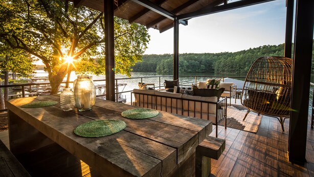 A wooden deck with a table set for dining, overlooking a lake with trees and hills in the background.