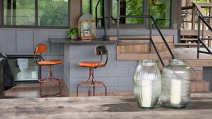 A modern outdoor seating area with two cushioned chairs, a lantern, and candles on a wooden table.
