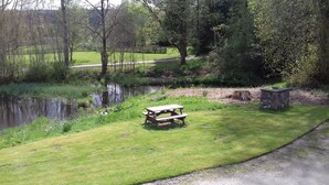 Een picknicktafel in een gazon, nabij een vijver, omringd door bomen en een stenen gebouw.